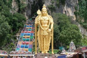 Majestic golden Lord Murugan statue stands before vibrant Batu Caves entrance in Selangor, Malaysia.